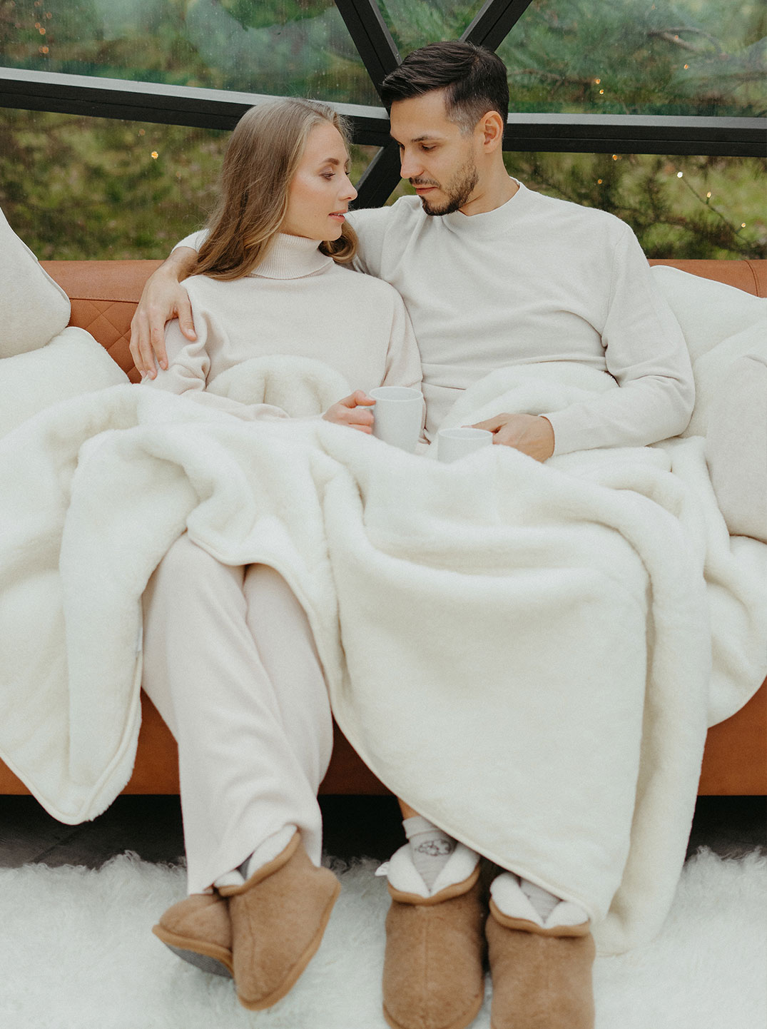 Ein Paar sitzt auf einem Sofa, eingekuschelt in eine weiße dicke Decke aus Merino-Kaschmir-Wolle