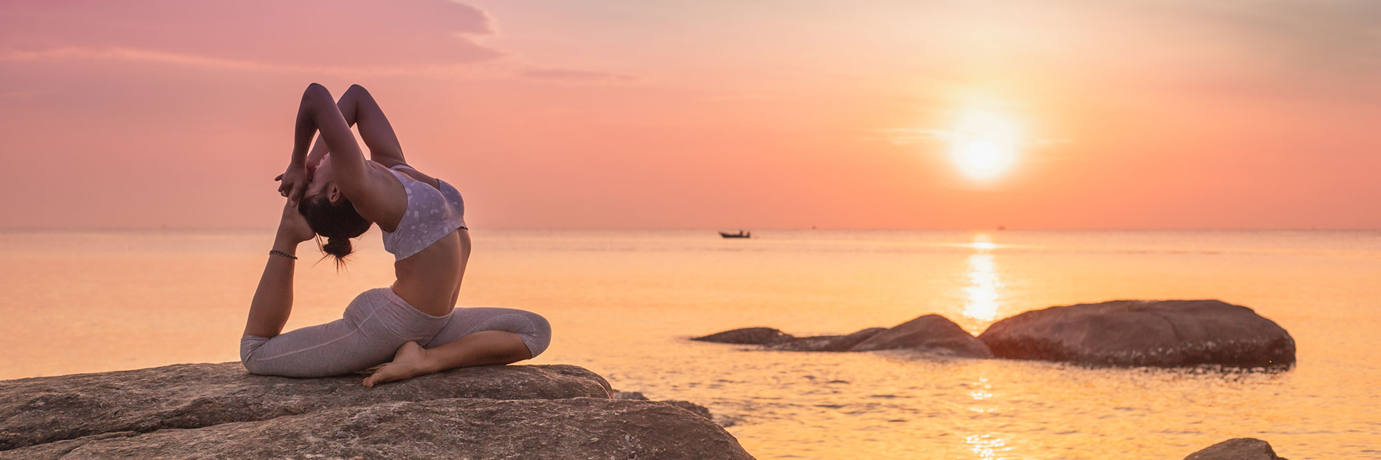 Frau praktiziert Yoga auf einem Felsen am Meer vor der untergehenden Sonne